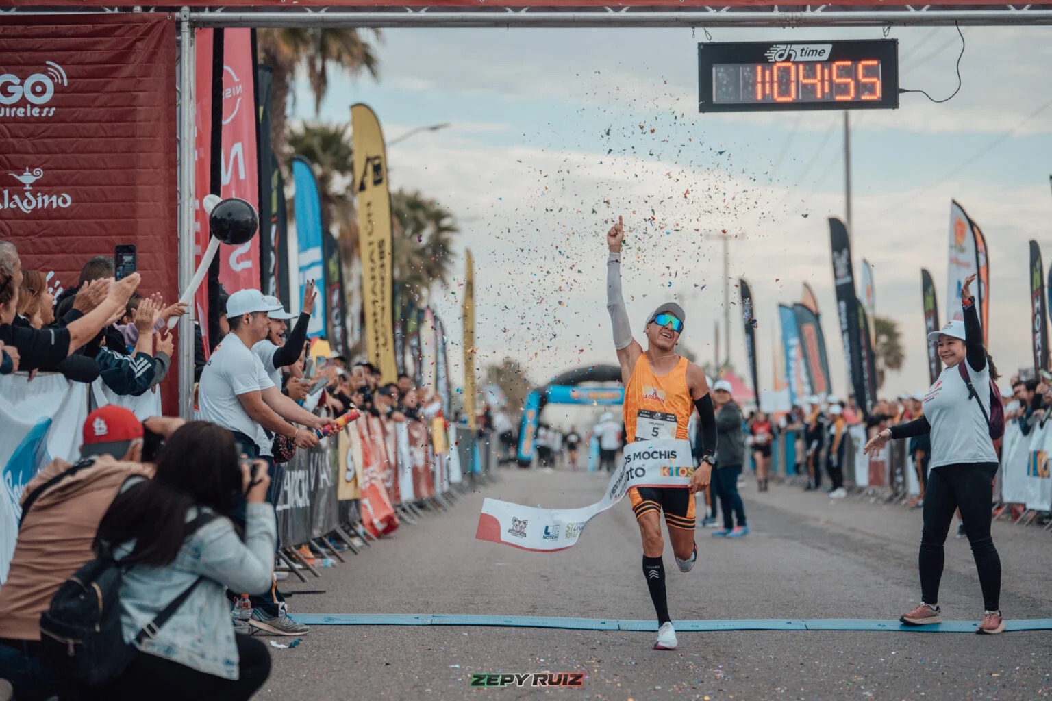 Corredor con playera naranja cruzando la meta del medio maratón de Los Mochis