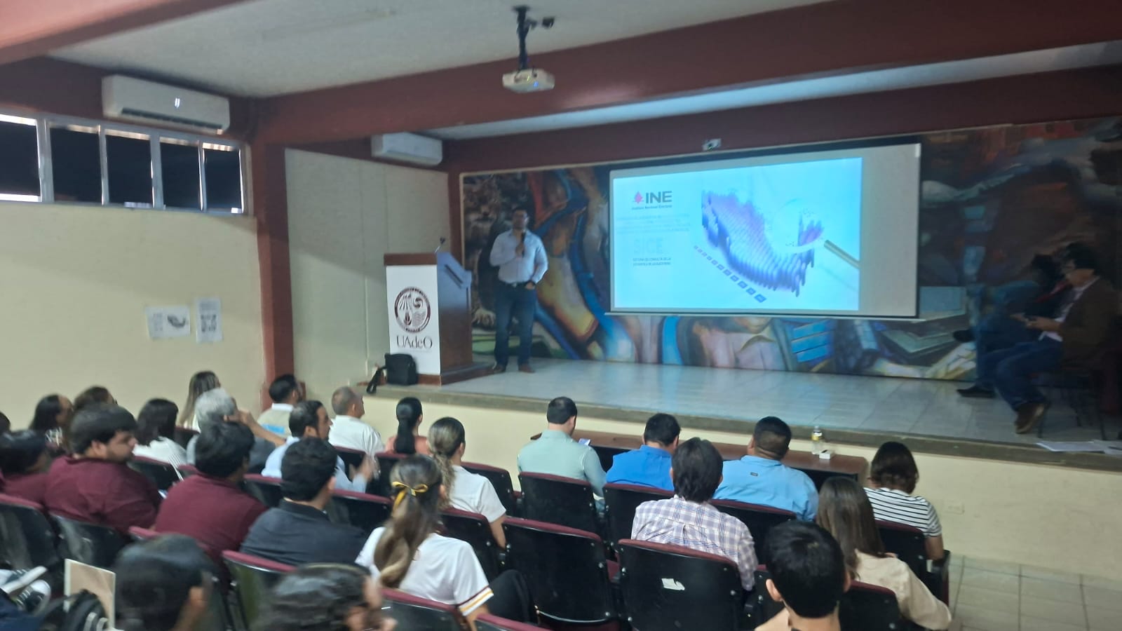 Conferencia de prensa con una proyección de un mapa en un auditorio