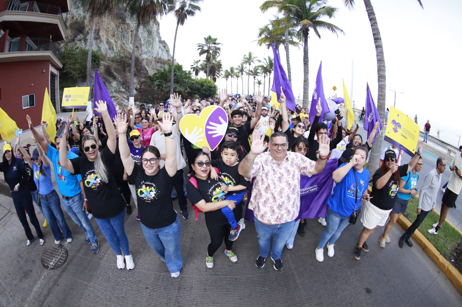 Personas con las manos levantadas caminando por la calle con logos de Teleton, banderas amarillas y moradas