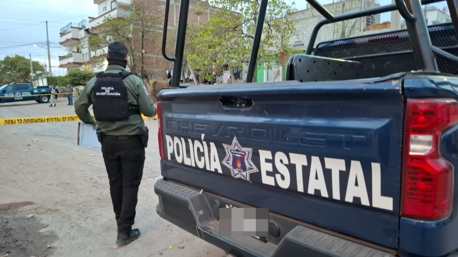 Parte trasera de camioneta de la Policía Estatal junto a un agente de investigación