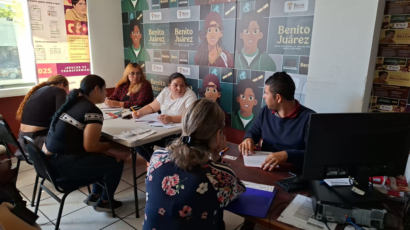 personas sentadas en mesa haciendo registro para beca