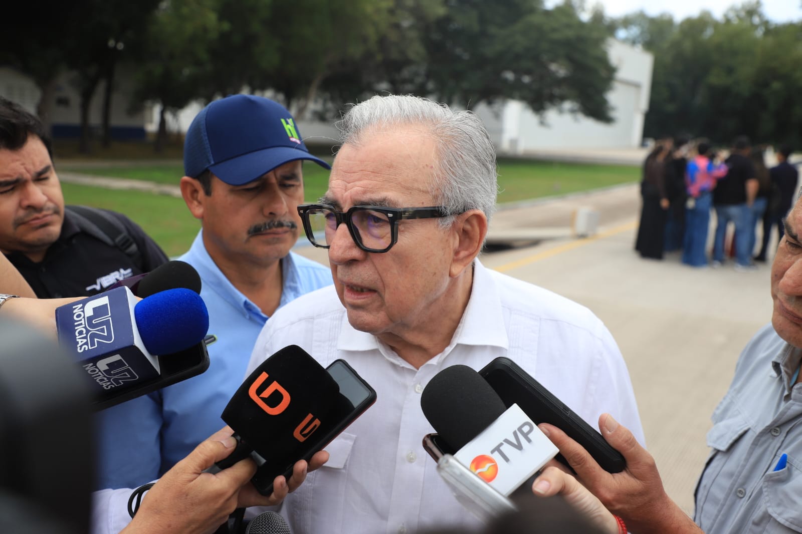 Rubén Rocha Moya hablando para micrófonos de noticieros y personas a su alrededor