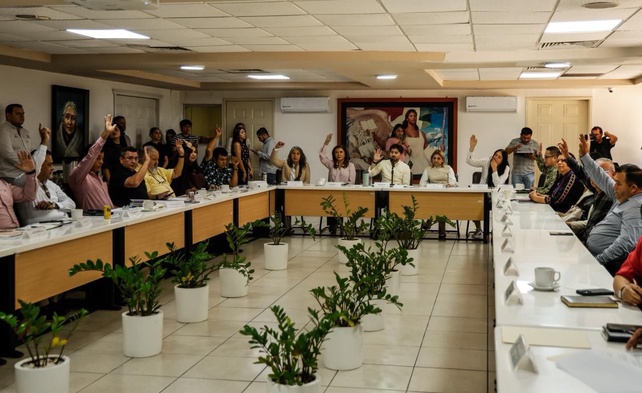 Reunión interinstitucional donde se autoridades sentadas en una mesa levantando la mano a manera de votación