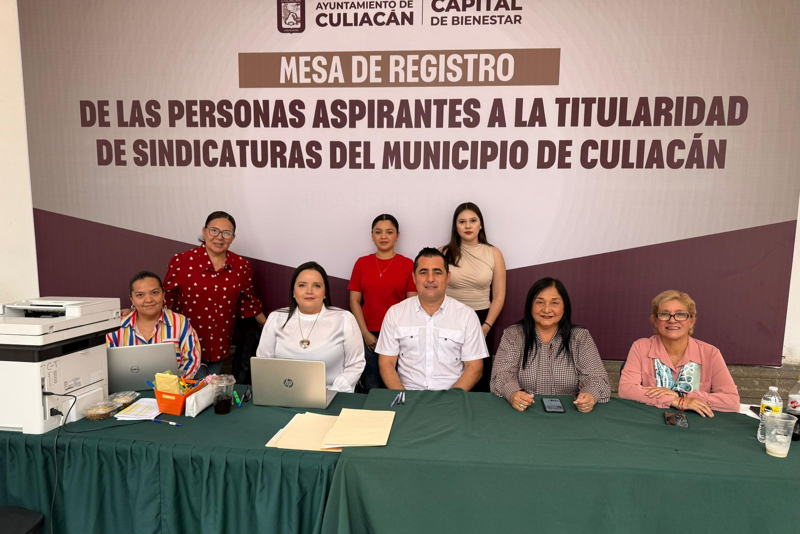 Personas en una mesa posando para la foto con un cartel detrás acerca de las sindicaturas