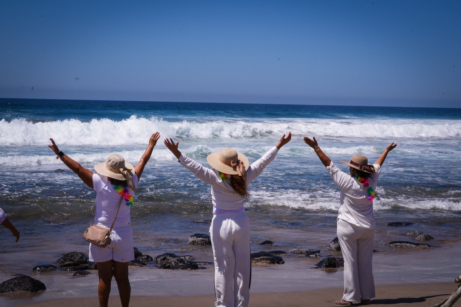Tres mujeres con los brazos abiertos frente a el mar