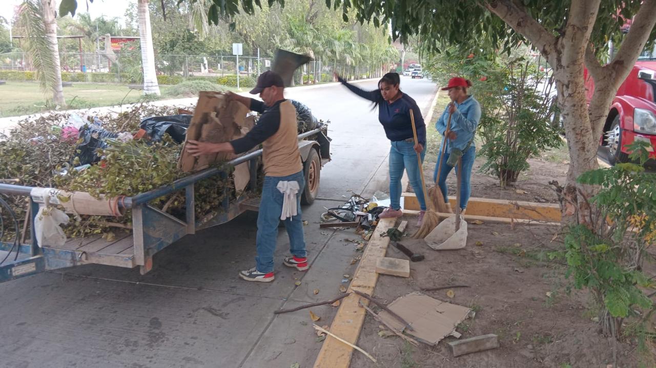Personas con herramientas de limpieza depositando basura en un remolque sobre una calle