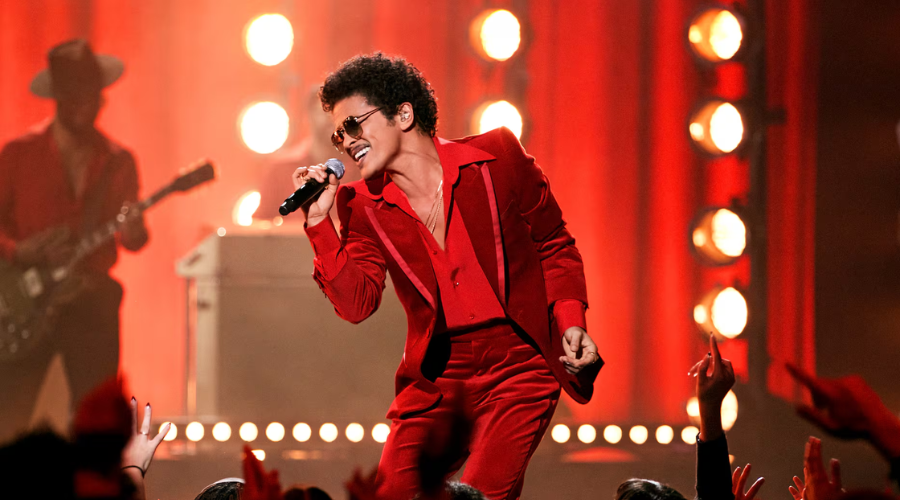 Bruno Mars vestido con un traje completo rojo cantando frente a miles de fanáticos con un micrófono