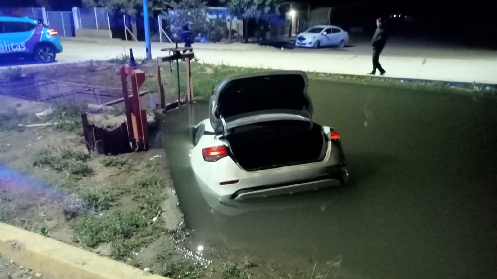 Carro de color gris con la cajuela abierta enn un canal