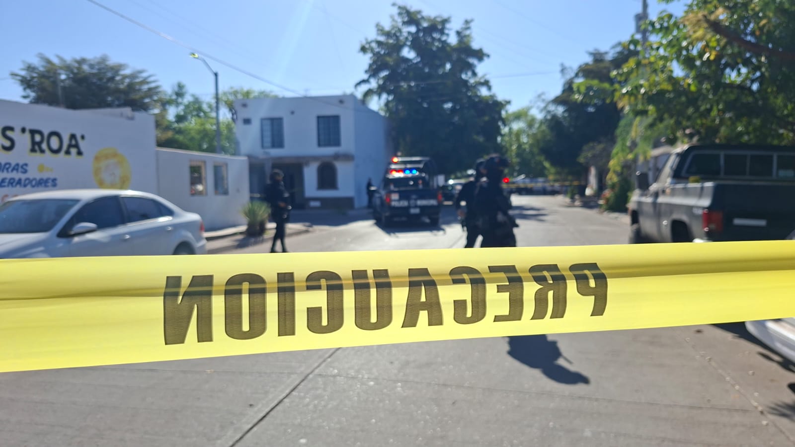Cinta amarilla de precaución en una calle y al fondo se observan dos unidades policiacas y elementos alrededor