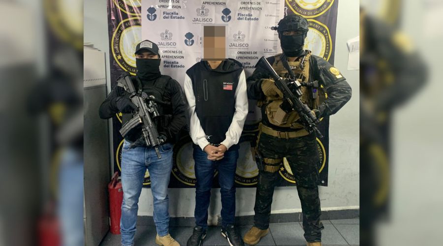 persona detenida con el rostro cubierto y ocn esposas en las manos, a los lados dos agentes de seguridad portando armas