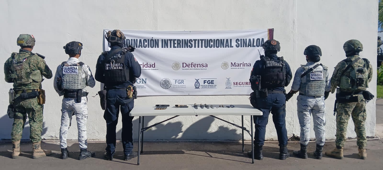 Elementos policiacos y en el medio una mesa con objetos y armas