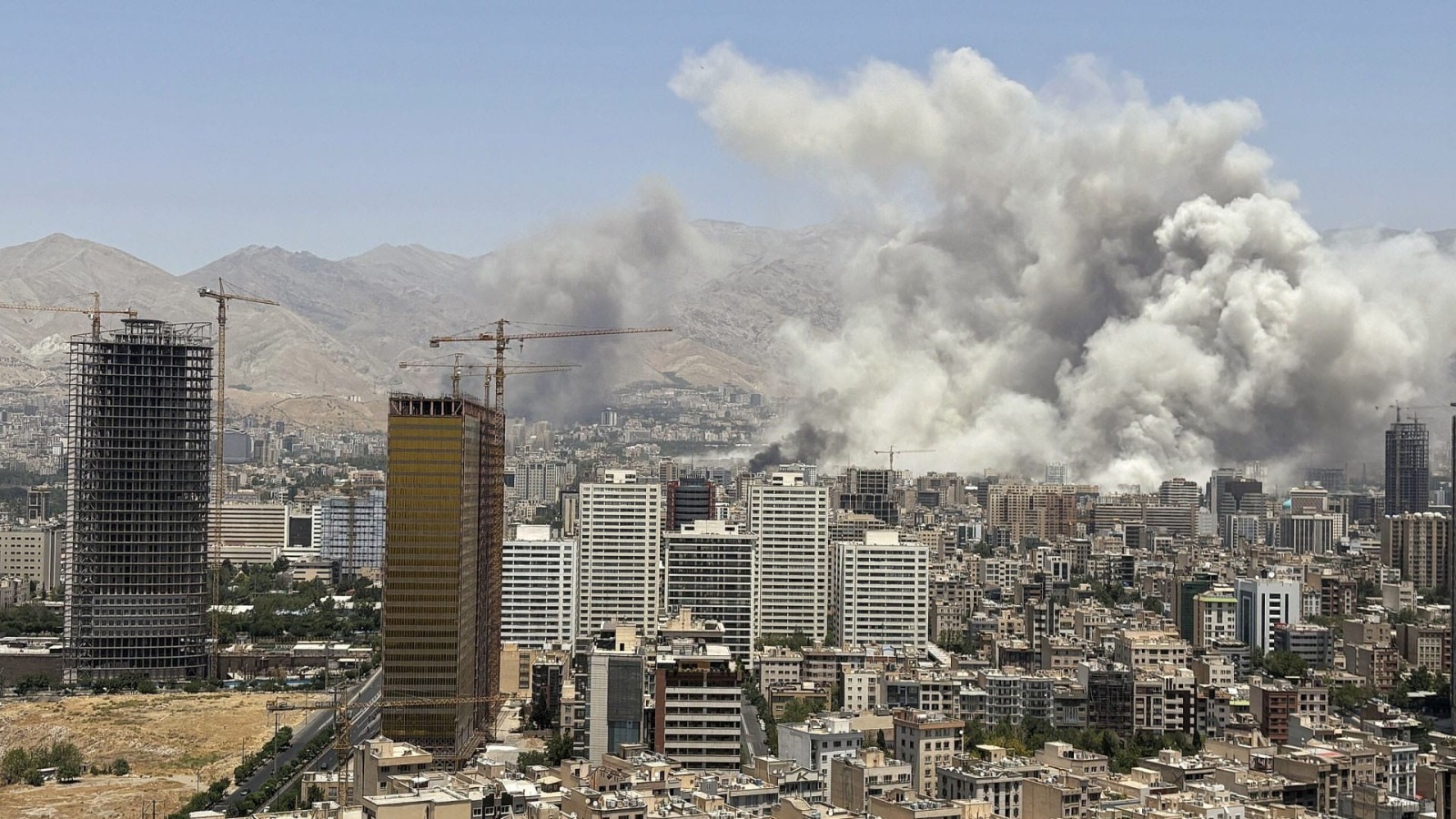 humo de explosión por guerra saliendo entre edificios altos en un día soleado