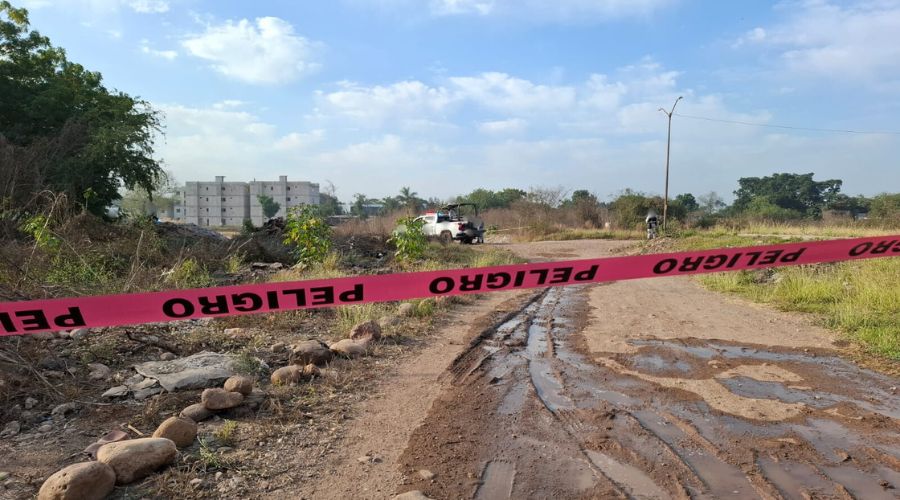 Cinta de precaución y a fondo una unidad policiaca y elemento desplegados en una zona de terracería o baldío