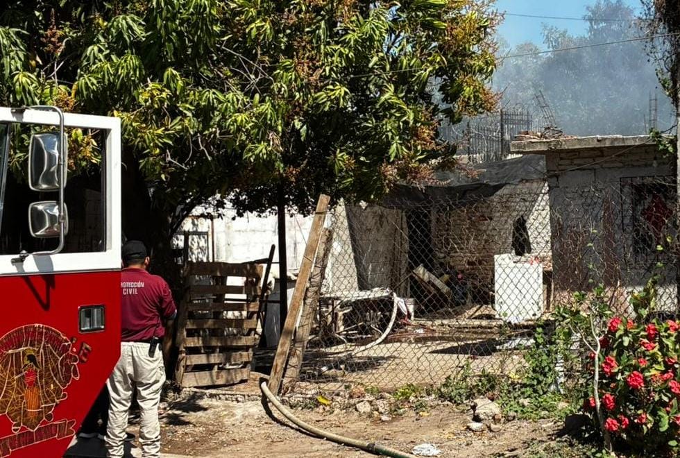 humo de incendio saliendo de la parte trasera de una casa, personal de bomberos de pie dando la espalda a la cámara