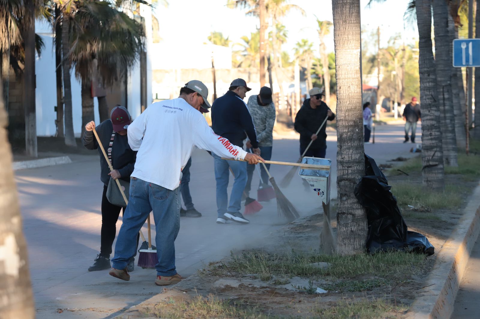 Personas realizando labores de limpieza con objetos como escobas y bolsas en una calle