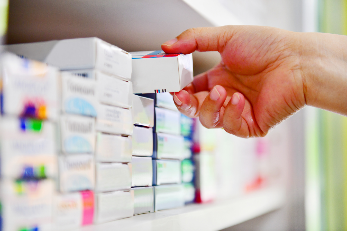 Estante con medicamentos y mano de una persona agarrando una caja
