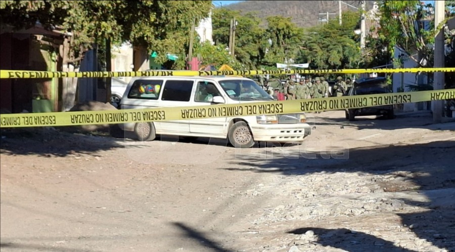 Cinta amarilla de precaución en un camino de terracería y militares al fondo