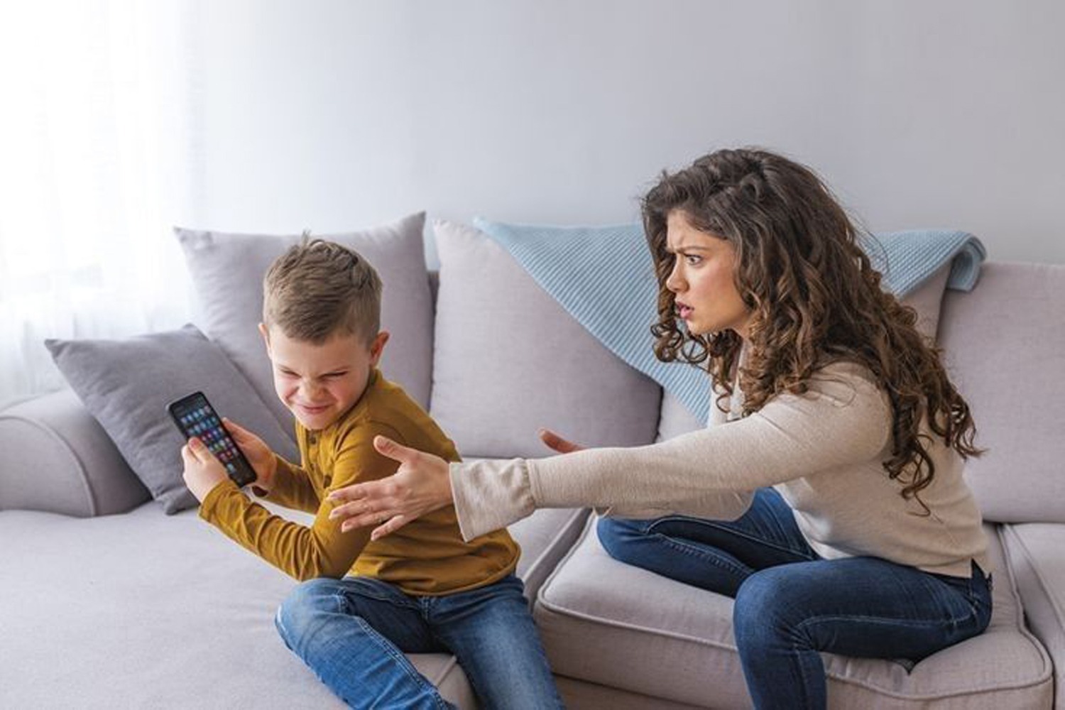 Niño con celular y persona adulta, ambos sentados en un sillón blanco