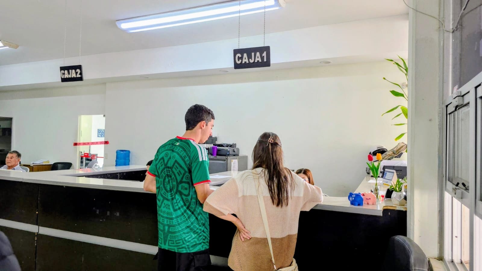 personas pagando en ventanilla de pago de espaldas a la cámara