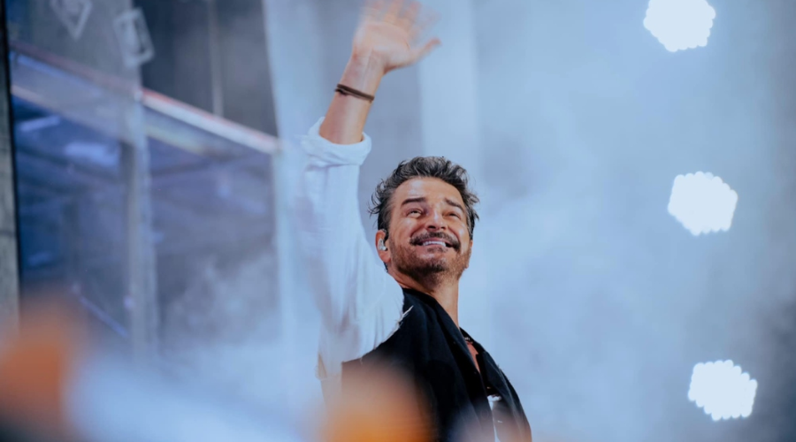 Ricardo Arjona levantando una mano con fondo azul y blanco