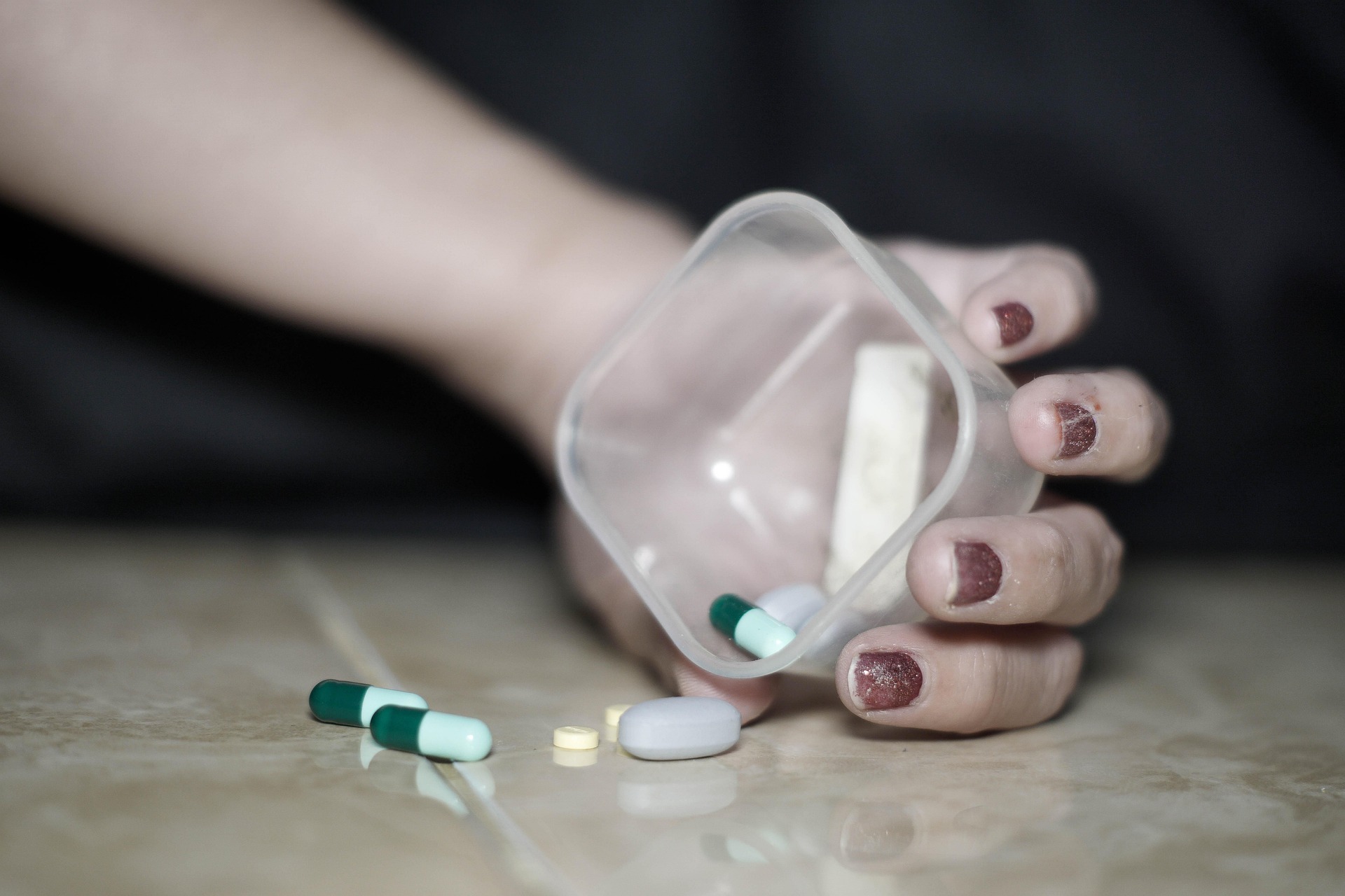 mano en el suelo con recipiente con pastillas
