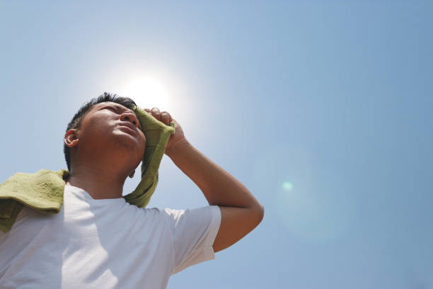 Persona sudando agarrando una toalla de tela y viendo hacia el cielo azul con un sol fuerte
