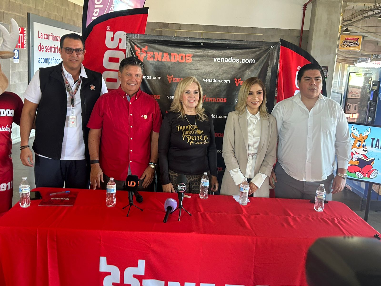 Personas en una rueda de prensa detrás de una mesa con un mantel rojo