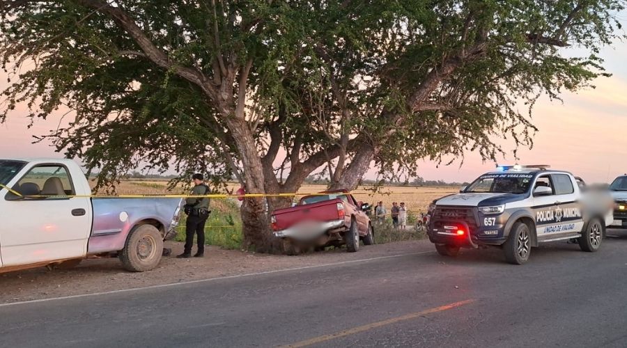 Camioneta chocada en un árbol junto a una camioneta de la policía y cinta amarilla de precaución