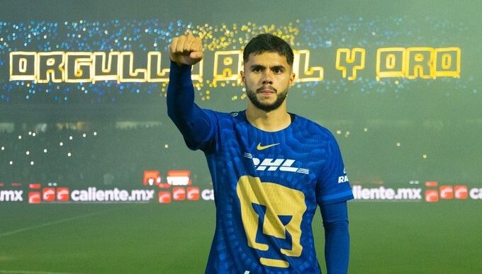 Alan Median con el jersey de Pumas y la mano derecha arriba con la mano en puño