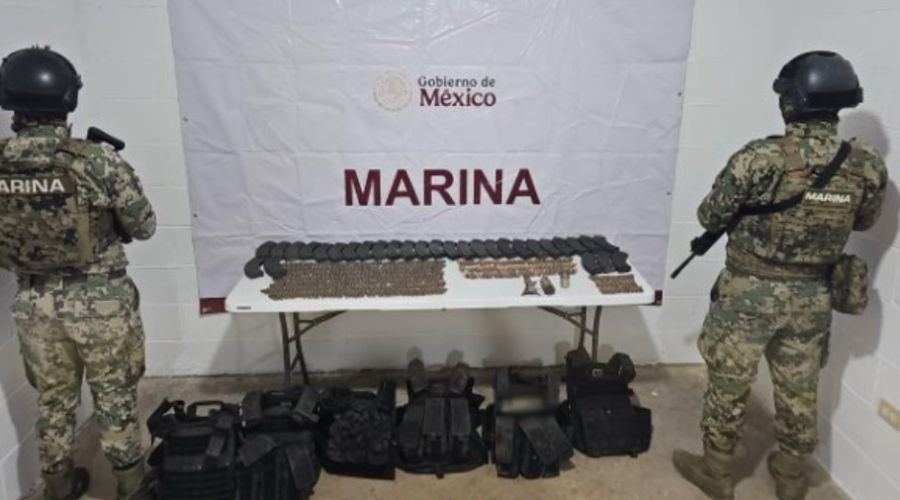 Elementos del ejercito de espaldas y en medio una mesa con artefactos confiscados, debajo, chalecos