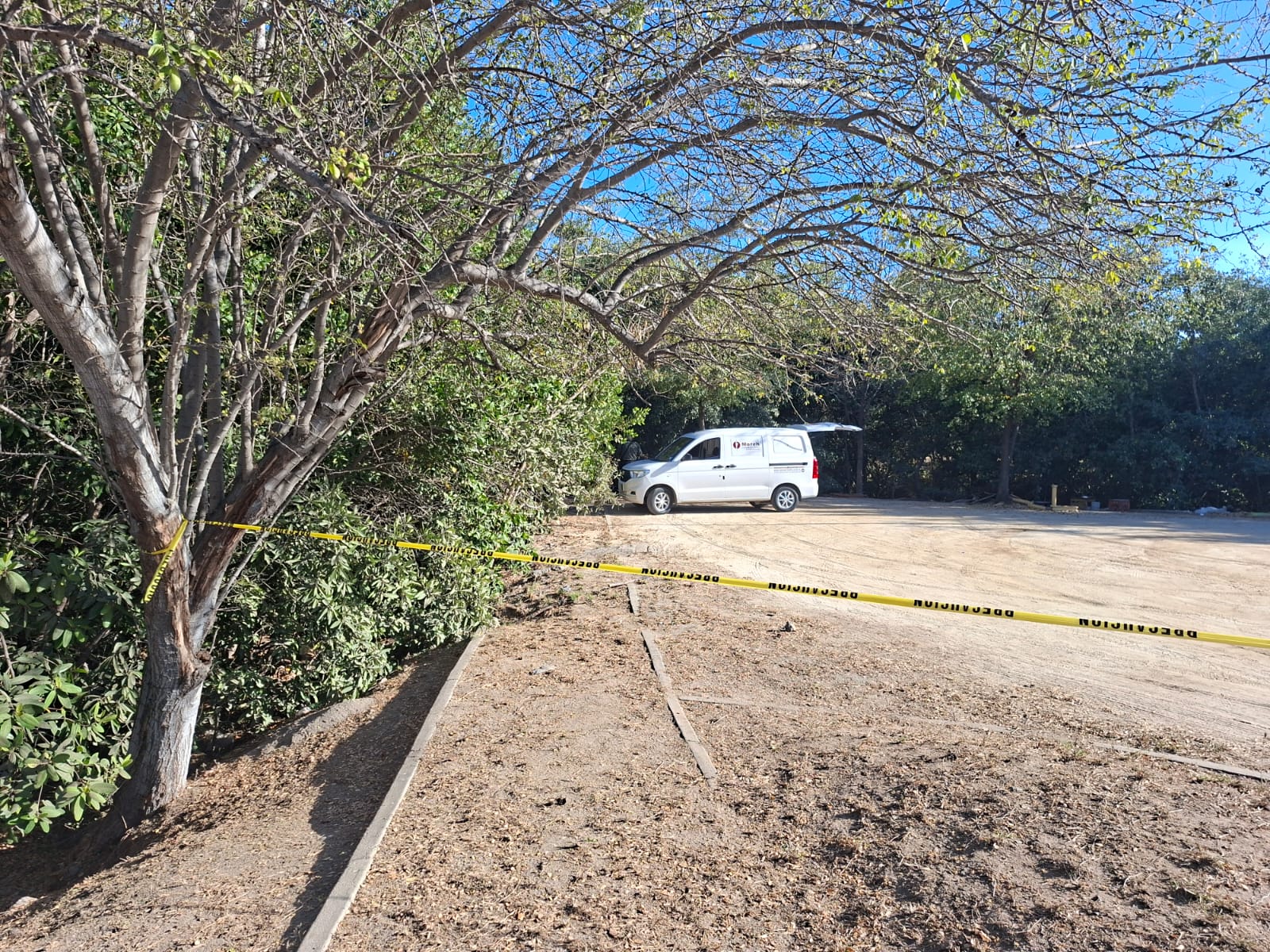 Arbustos con una cinta amarilla de precaución junto a una camioneta blanca de la Moreh