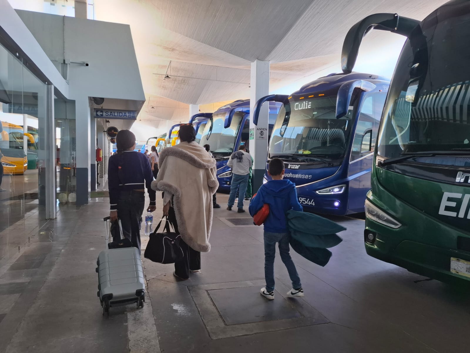 Personas caminando con maletas por una central donde se ve autobuses estacionados