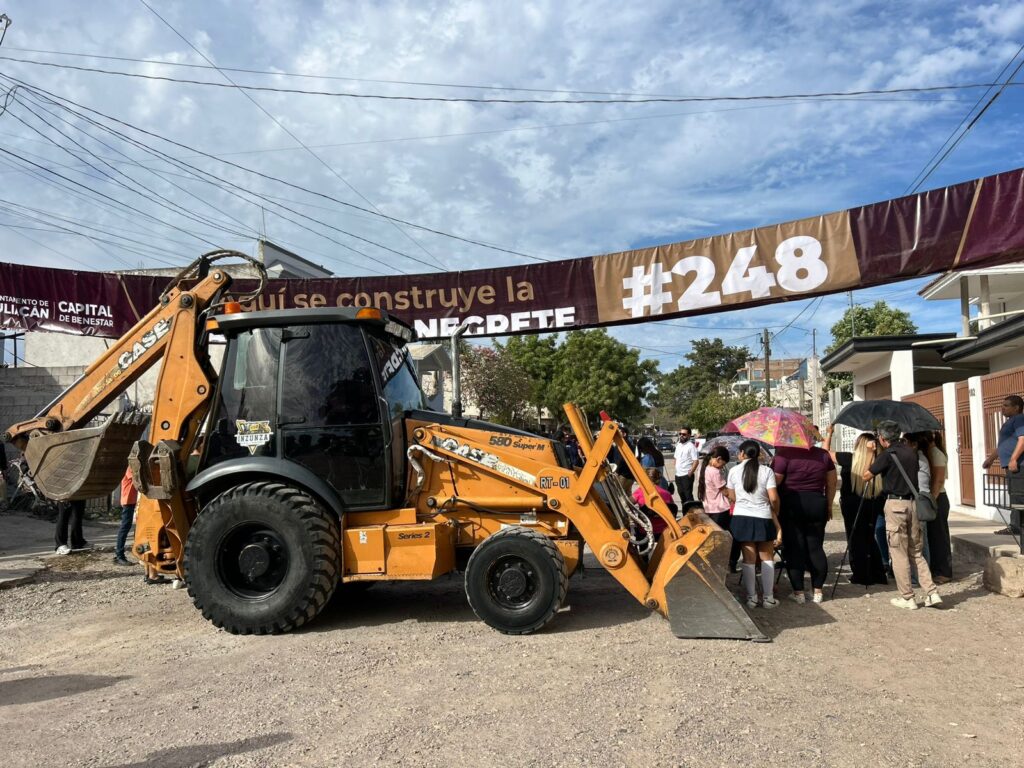 Máquina pesada de construcción junto a autoridades y una lona arriba de ella