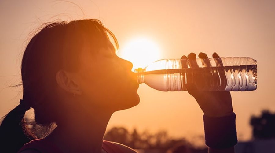 Mujer tomando de una botella de agua, mientras le pega el sol de lado