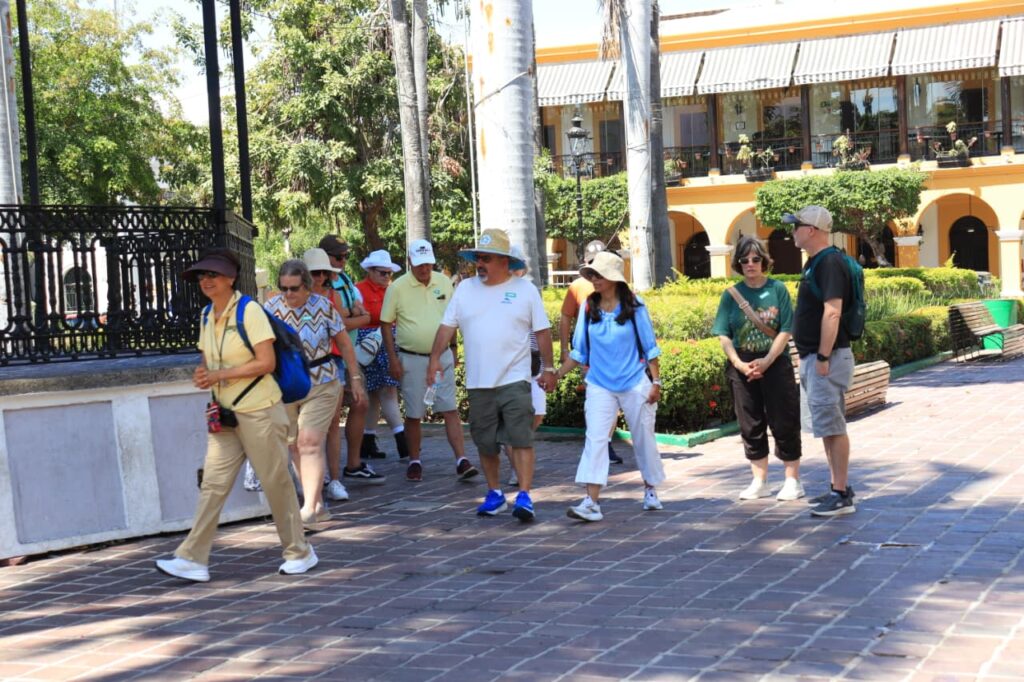 Turistas en Mazatlán en un kioso de una plaza junto a un guía de un tour