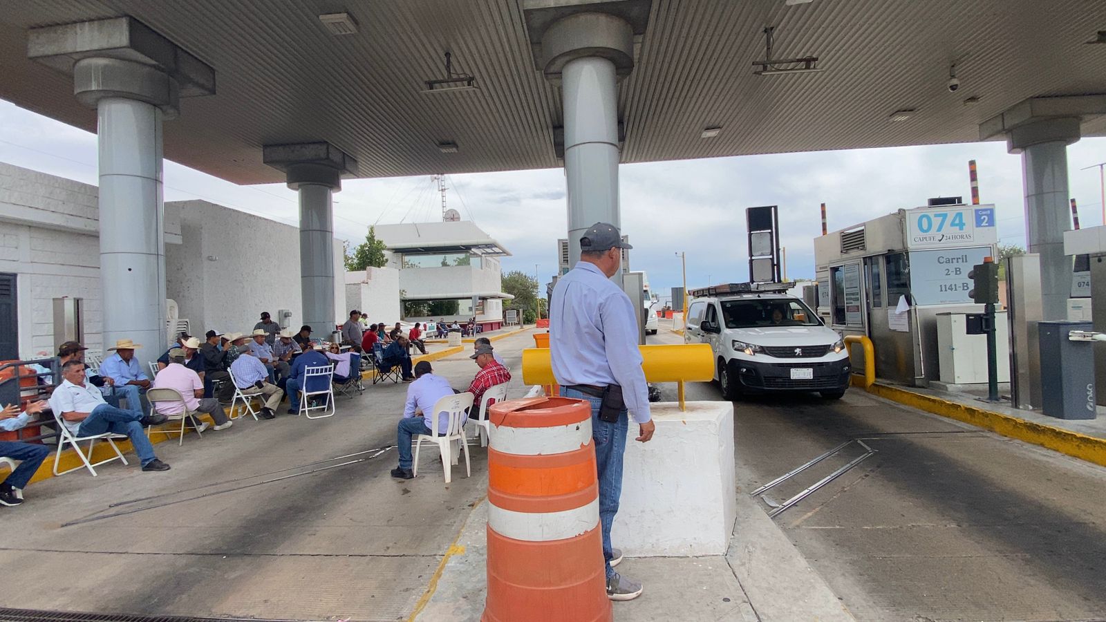 Personas sentadas debajo de la caseta de cobro junto a un tráiler