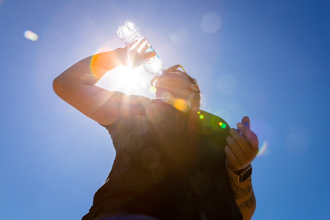 Cielo azul con sol y persona tomando agua
