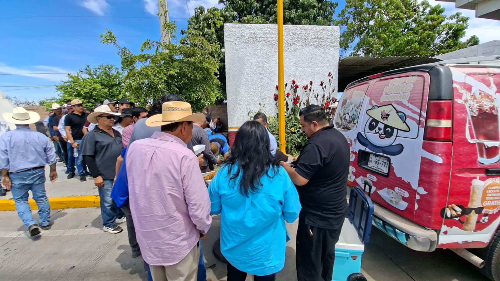 Personas reunidas junto a una camioneta roja con una persona con ropa color negro entregando comida