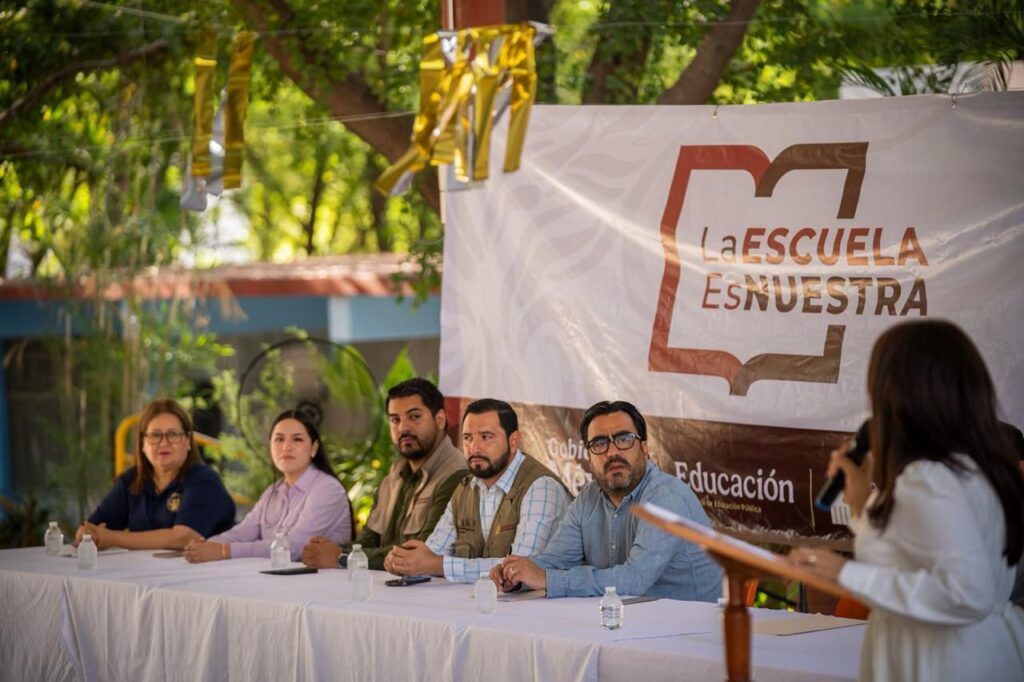 Juan de Dios Gámez sentado en evento de la Escuela es nuestra junto a autoridades