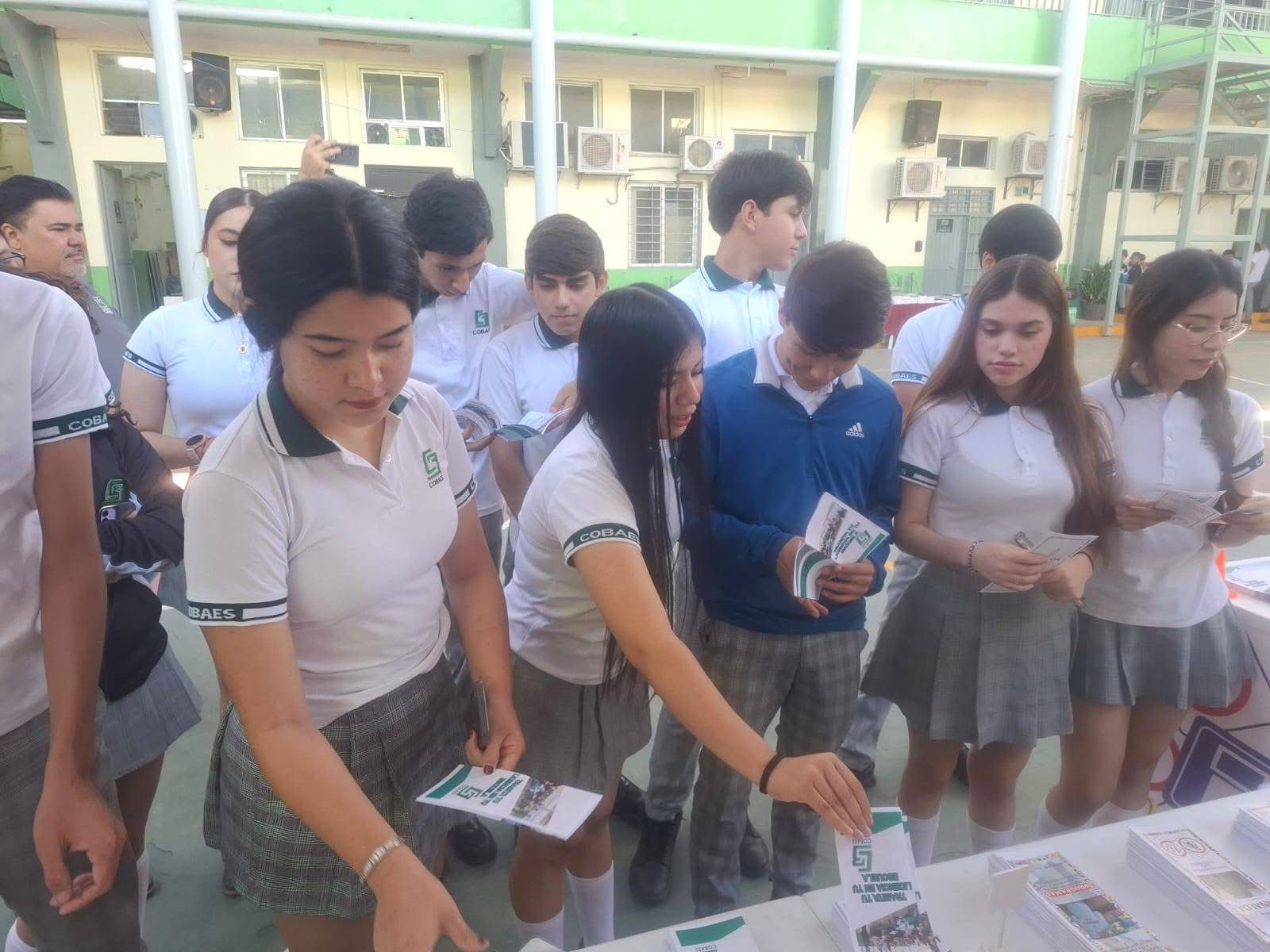 adolescentes de preparatoria detrás de mesa con folletos