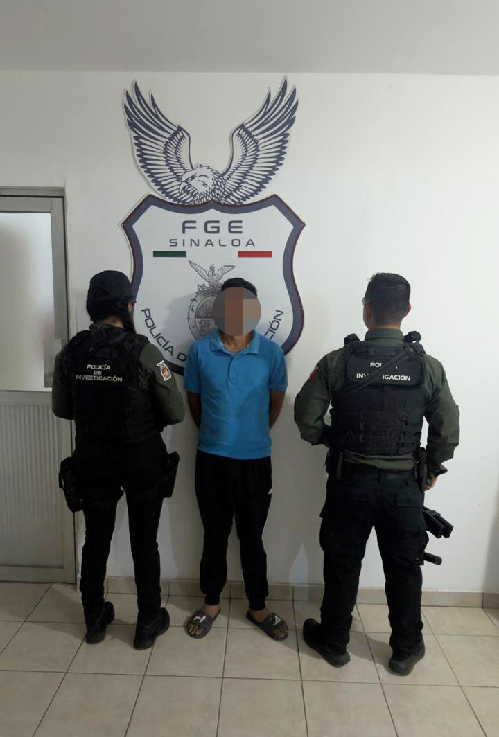 Una persona con camisa color azul con la cara difuminada junto a dos elementos de seguridad en una pared blanca