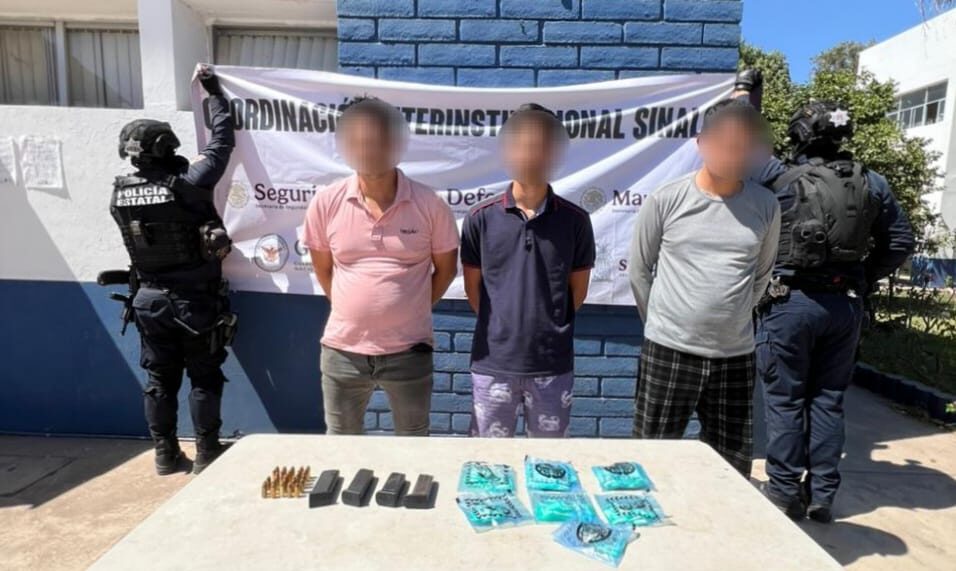 Tres personas detenidas con la cara difuminada y una mesa con bolsas y cargadores y elementos de seguridad a los costados