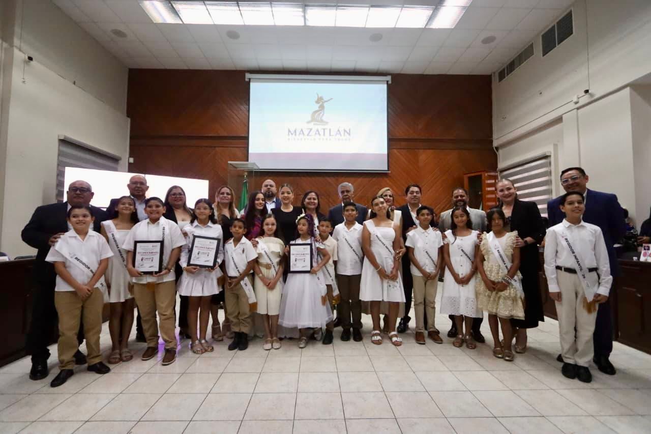 Niños y Adultos formados posando para foto con proyector e imagen de Mazatlán detrás de ellos