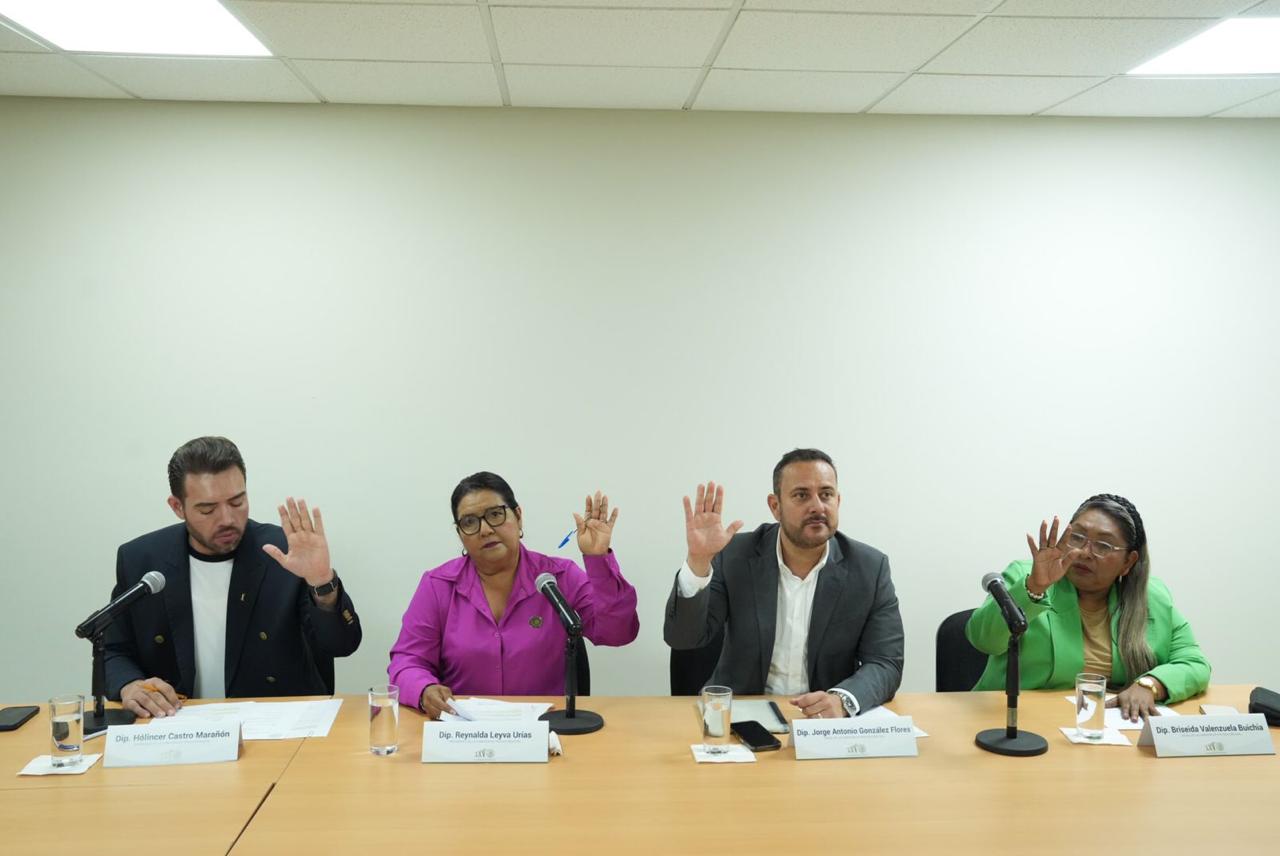 Diputados en una mesa con la mano derecha levantada a manera de votación