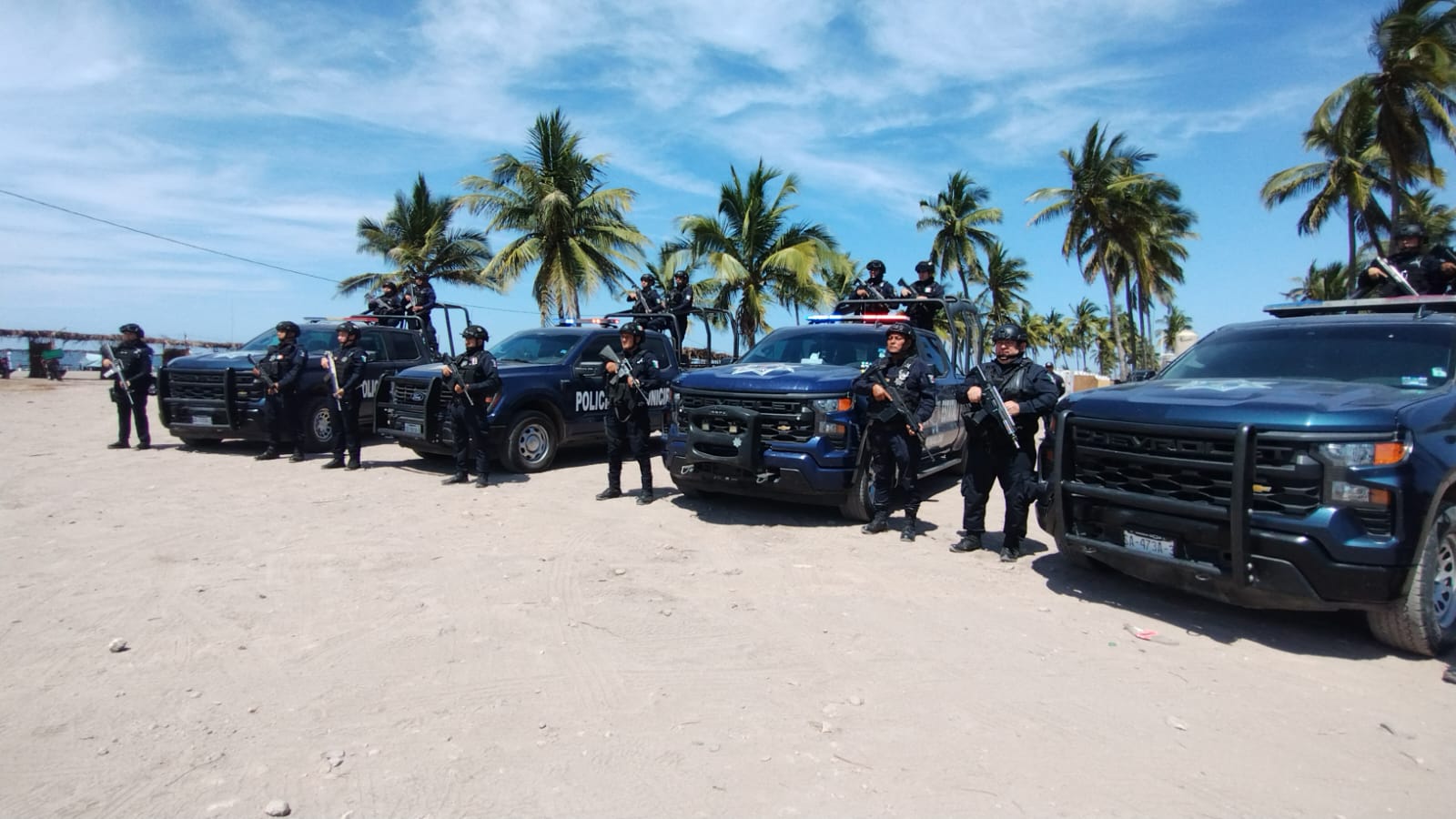 policías uniformados y con armas formados a lado de patrullas en la playa