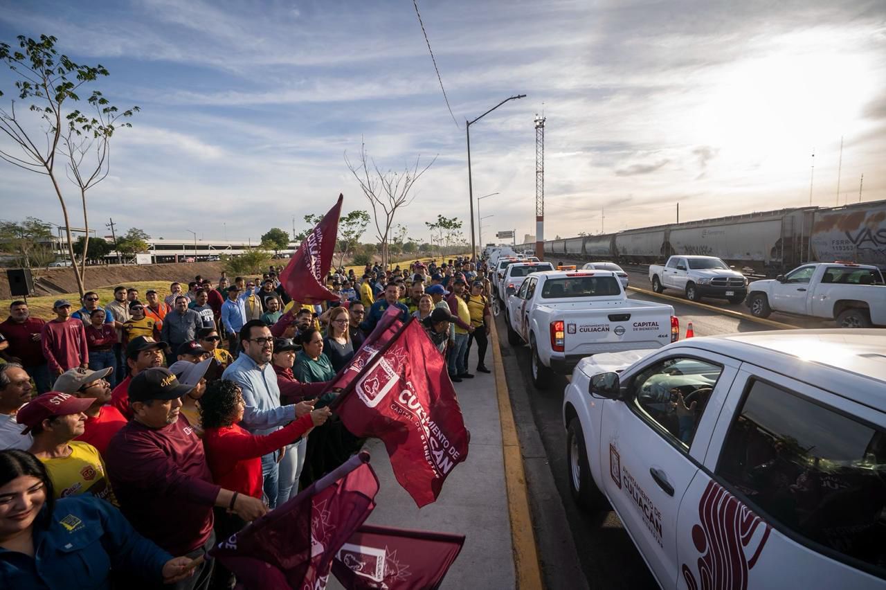 Ciudadanos y autoridades sosteniendo banderas y frente a ellos vehículos