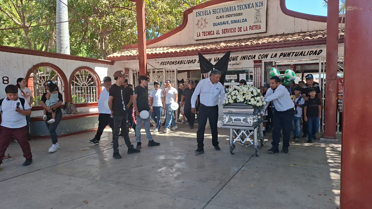 Alumnos y autoridades de ETI 28 junto a un ataúd con flores y un moño negro