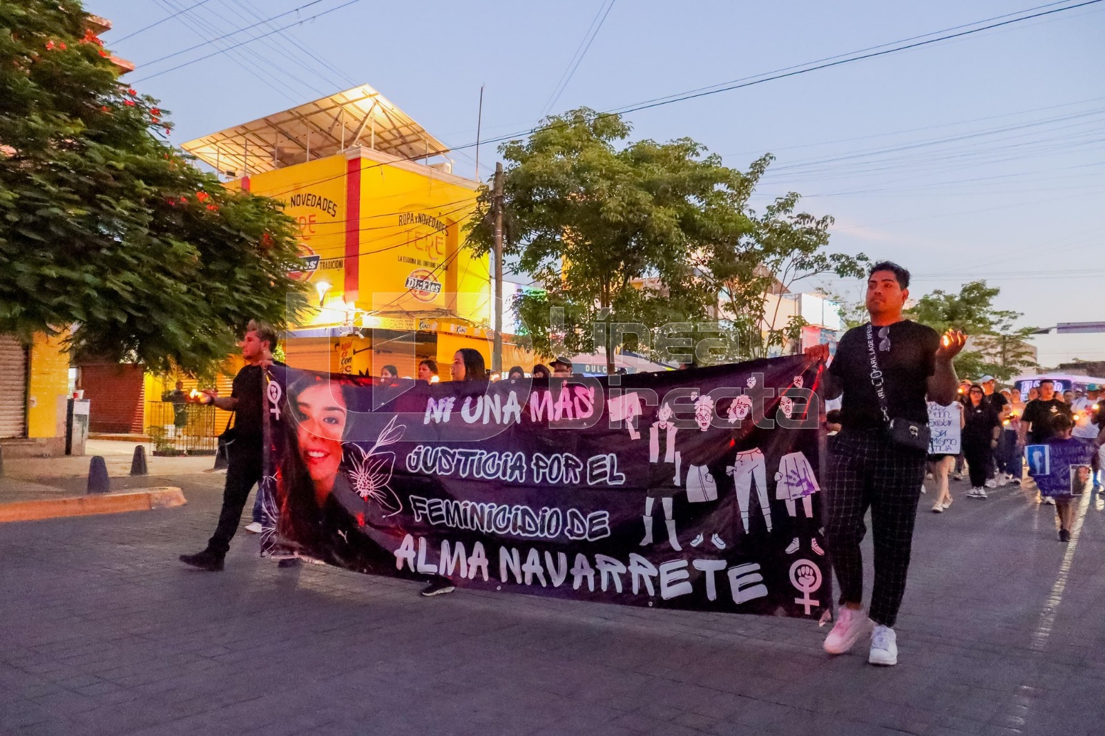 Dos personas marchando con una lona de feminicidio de Alma Navarrete
