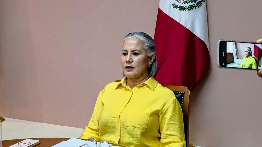 Mujer sentada en una oficina con una bandera de México atrás de lla