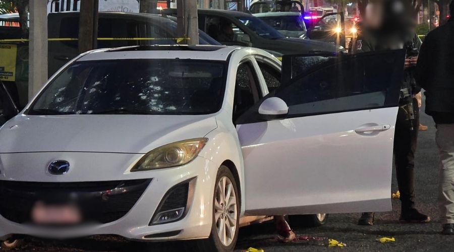 Carro color blanco con la puerta abierta e impactos de bala en el cristal